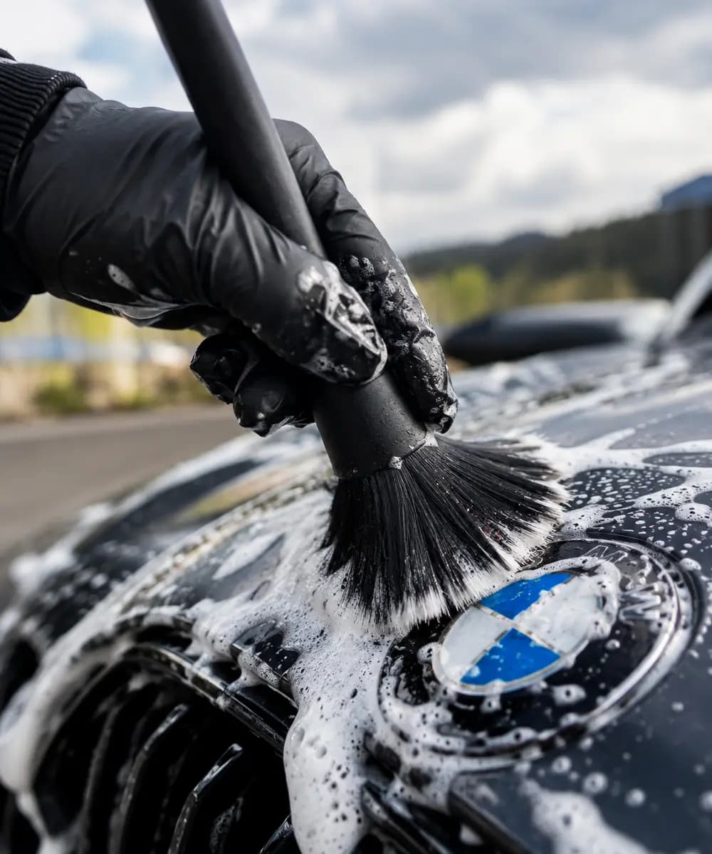 Ruka v rukavici čistí kartáčkem zpěněný znak BMW na kapotě