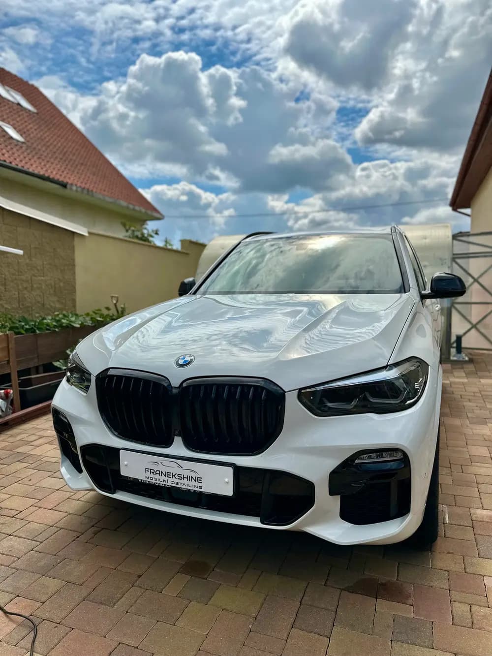Bílé BMW X5 zepředu na dvorku po umytí a naleštění