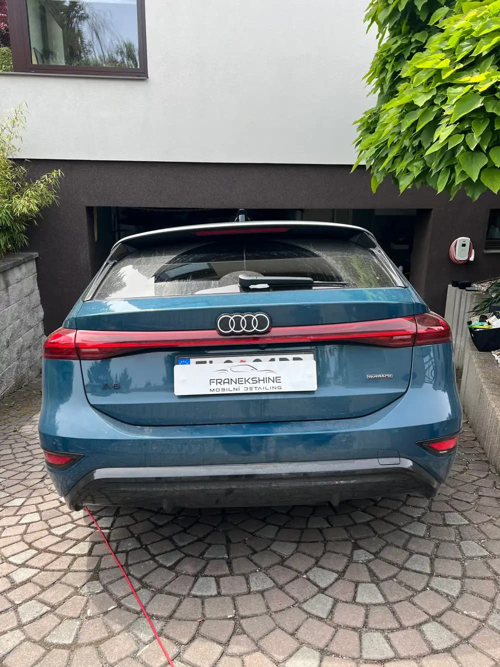 Modré kombi Audi A6 zezadu před garáží s nabíjecí stanicí