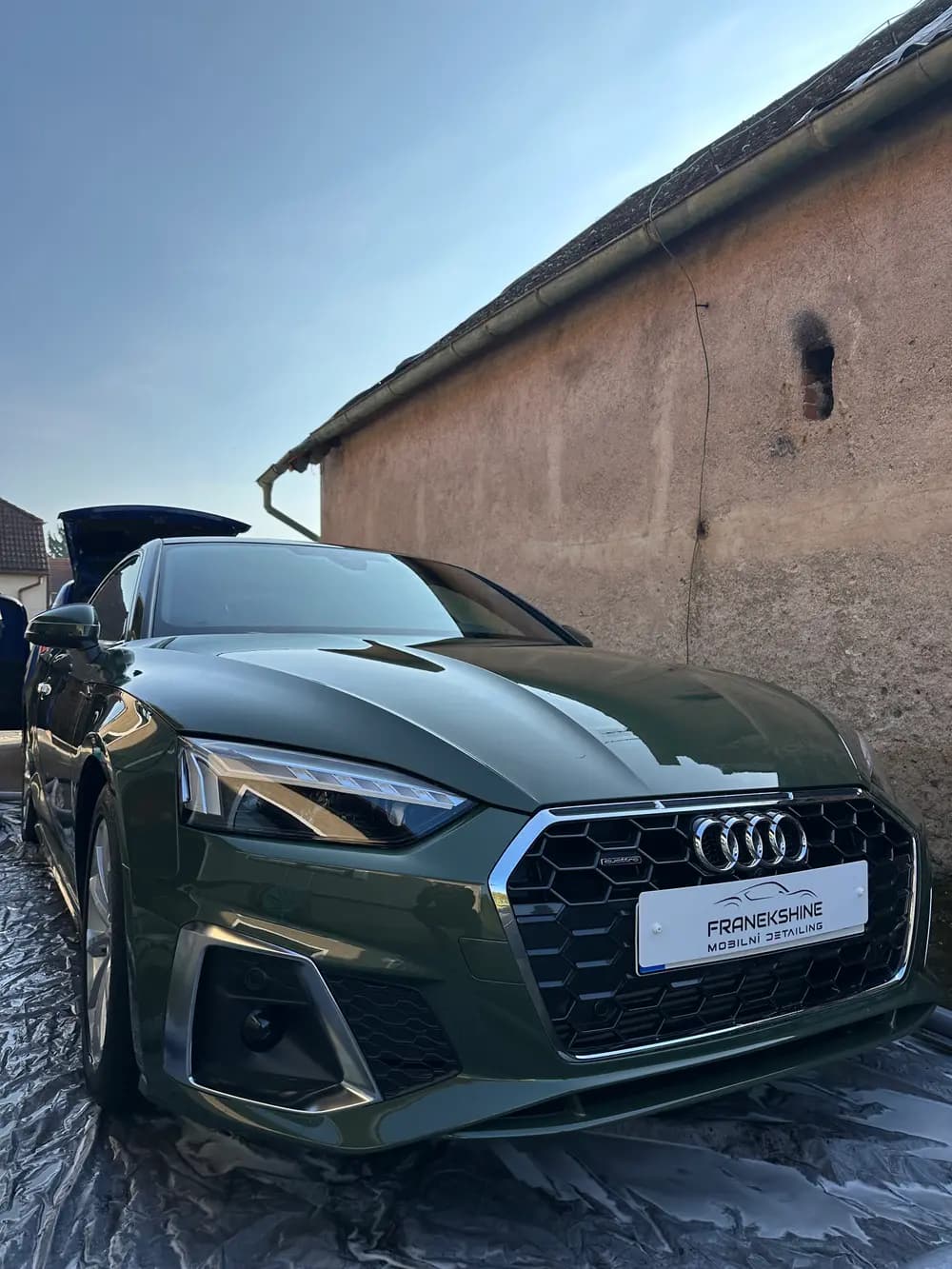 Zelené Audi A5 z boku s otevřeným kufrem u kamenné zdi