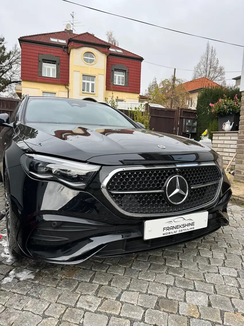 Černý Mercedes s ještě vlhkou kapotou po umytí před vilou s červenou střechou