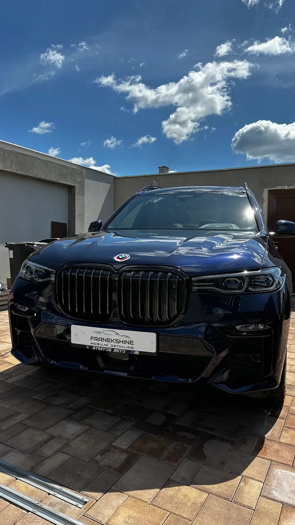 Detail masky modrého BMW X7 M pod dramatickou oblohou